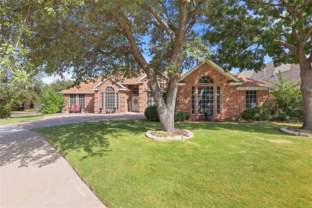 1926 Vintage Drive, Corinth, TX 76210 Red brick facade with arched window, established front yard, mature trees, and a concrete driveway