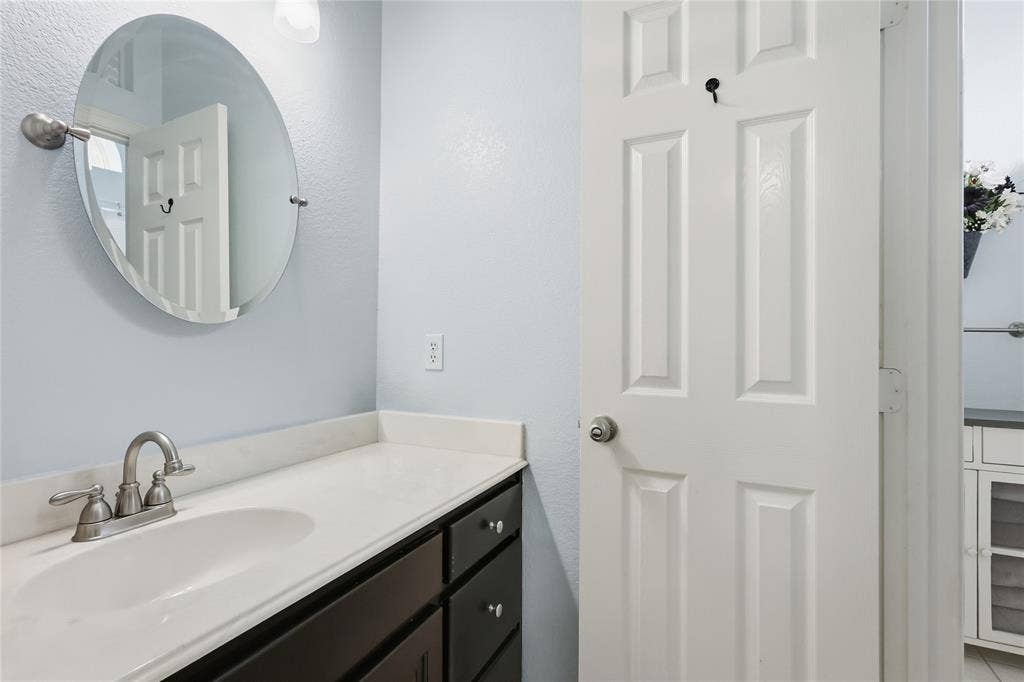 1926 Vintage Drive, Corinth, TX 76210 Vanity with an integrated sink, brushed nickel faucet, dark wood-finish cabinetry, and a round wall-mounted mirror