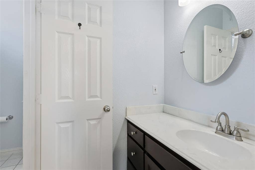 1926 Vintage Drive, Corinth, TX 76210 White countertop with integrated sink, dark wood-finish vanity, brushed nickel faucet, and oval wall-mounted mirror