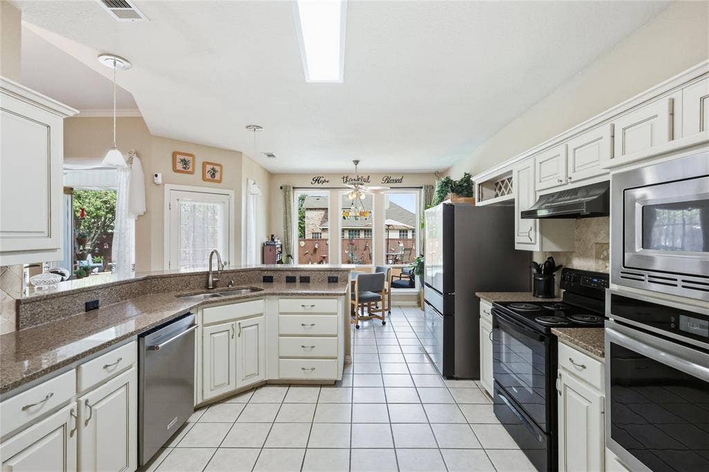1926 Vintage Drive, Corinth, TX 76210 White cabinetry with brushed nickel hardware, granite-look countertops, stainless steel appliances, tiled flooring, and ample natural light