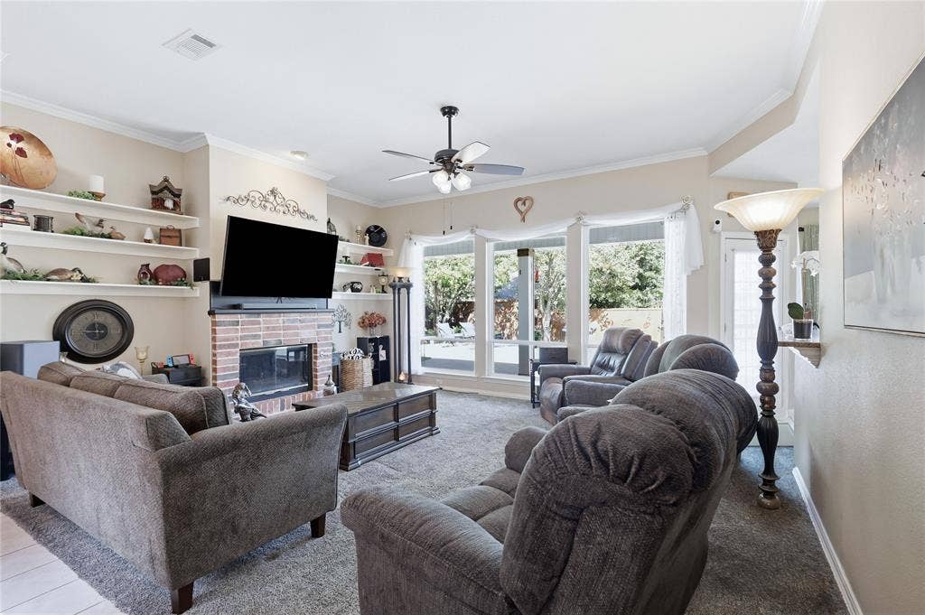 1926 Vintage Drive, Corinth, TX 76210 Brick fireplace with a built-in television mount, integrated shelving, crown molding, a ceiling fan, and large windows