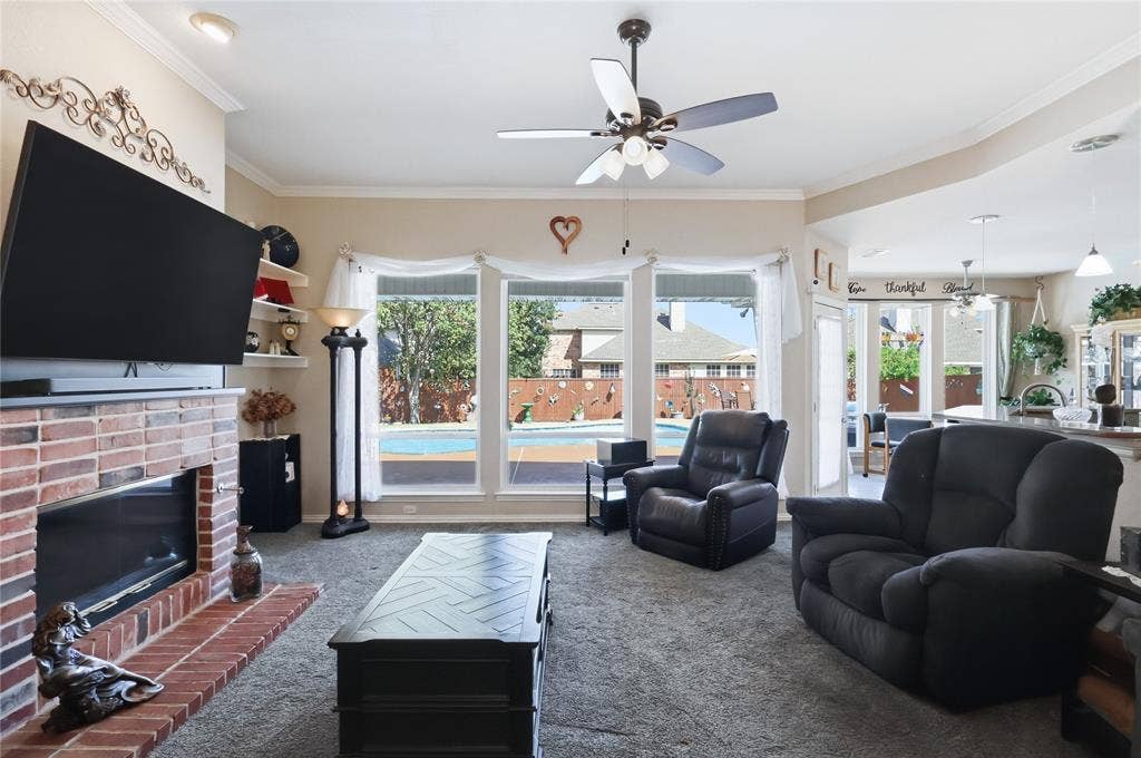 1926 Vintage Drive, Corinth, TX 76210 Living area with a brick fireplace, built-in shelving, ceiling fan, and large windows overlooking a backyard pool