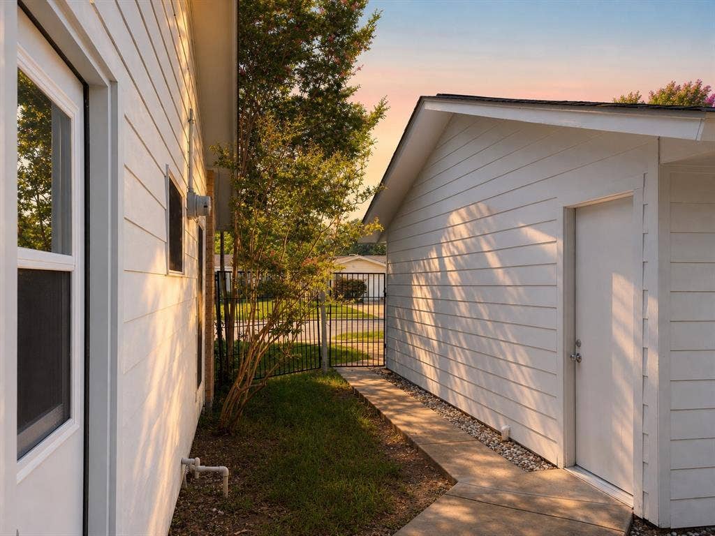 3401 Hanover Lane, Irving, TX 75062 White horizontal siding exterior with a concrete walkway, black metal fencing, and a separate structure featuring a side-entry door