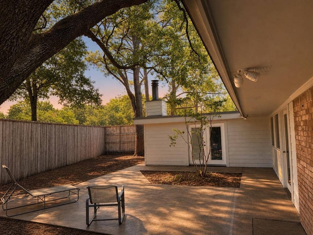 3401 Hanover Lane, Irving, TX 75062 Expansive concrete patio with direct access to interior spaces, bordered by a privacy fence, with a separate exterior building featuring a single glass-paneled door