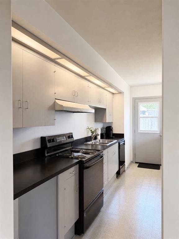 3401 Hanover Lane, Irving, TX 75062 Galley kitchen featuring ample upper and lower cabinetry, dark countertops, a stainless steel sink, and a full-size electric range