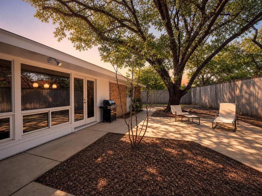 3401 Hanover Lane, Irving, TX 75062 Expansive concrete patio with mature tree, wood fence, and large window panels