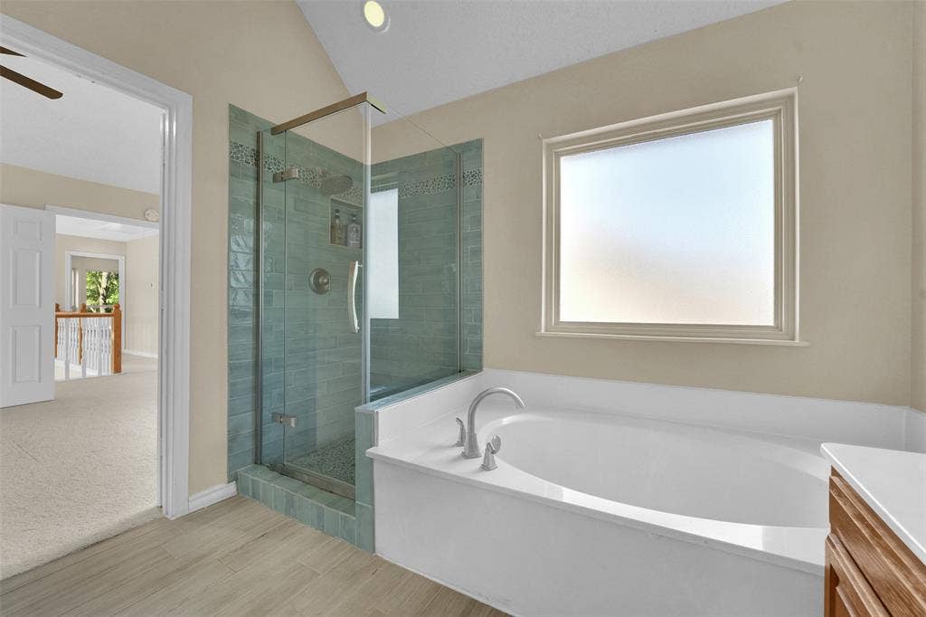 1920 Keystone Drive, Plano, TX 75075 Soaking tub with brushed nickel fixtures, a glass-enclosed shower with blue-toned tile, and wood-finish flooring