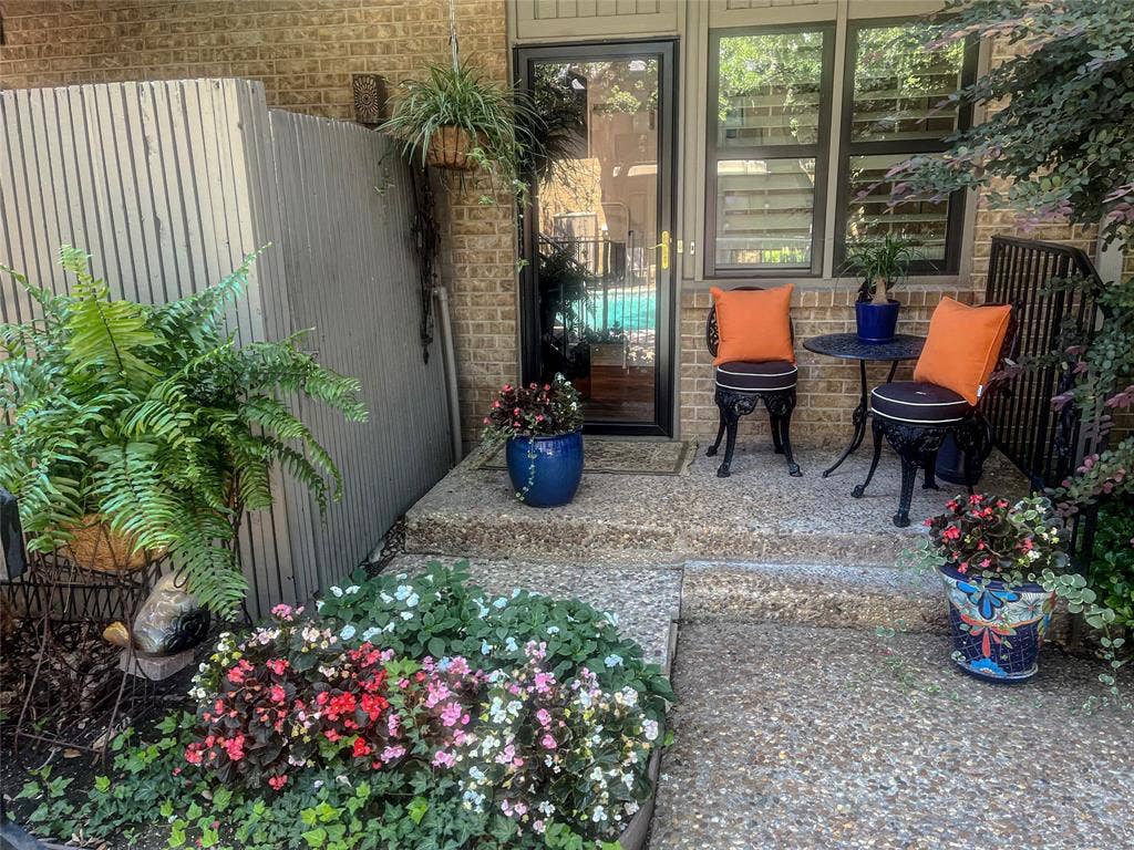10719 Villager Road, #A, Dallas, TX 75230 Brick exterior with a glass-paneled entry door, adjacent windows with interior shutters, and an exposed aggregate concrete patio