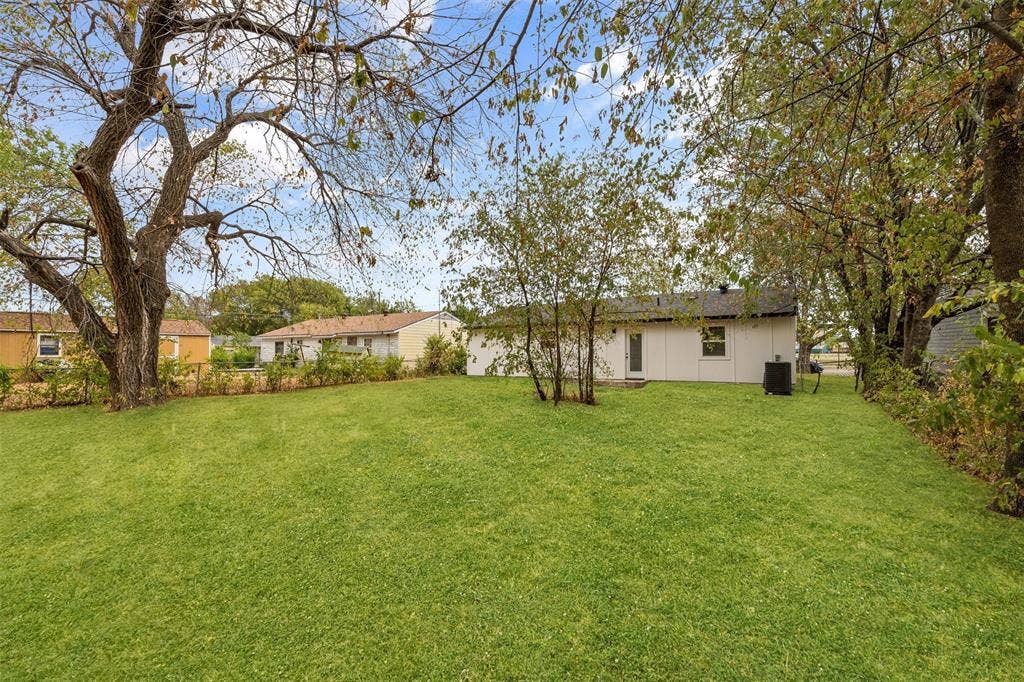 565 alcorn Avenue, Dallas, TX 75217 Expansive green lawn with mature trees and a single-story residence featuring a dark roof
