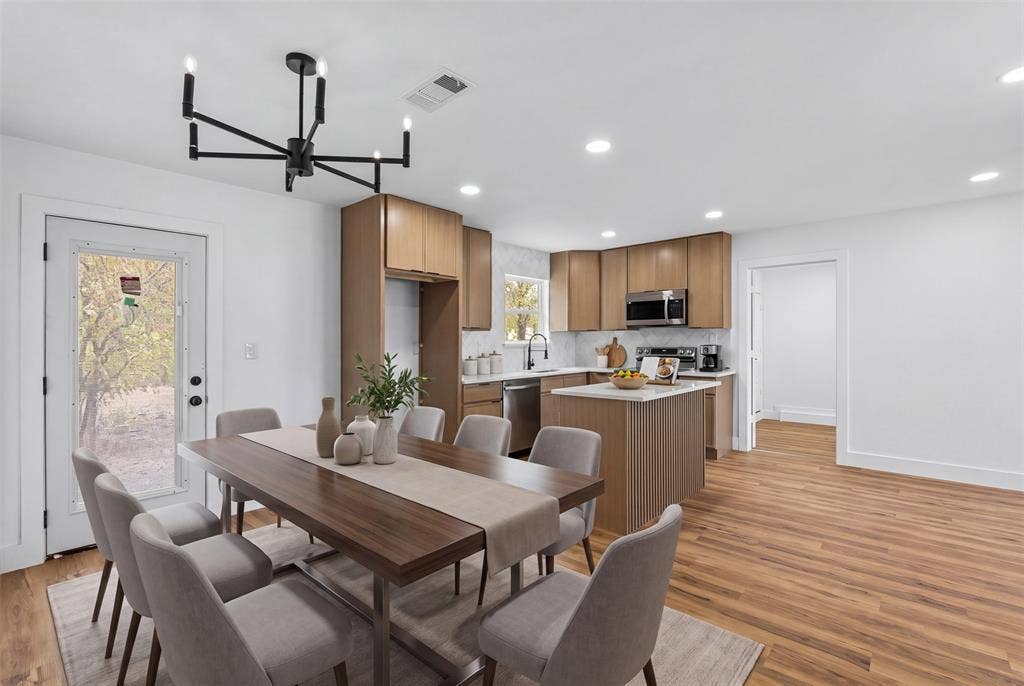 565 alcorn Avenue, Dallas, TX 75217 Open-concept living area featuring wood-finish flooring, a modern chandelier, light wood cabinetry, white countertops, and a full-light exterior door