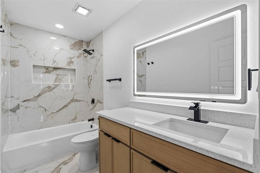 565 alcorn Avenue, Dallas, TX 75217 Tiled shower with a niche, tub, wood-finish vanity, integrated sink, and an illuminated mirror