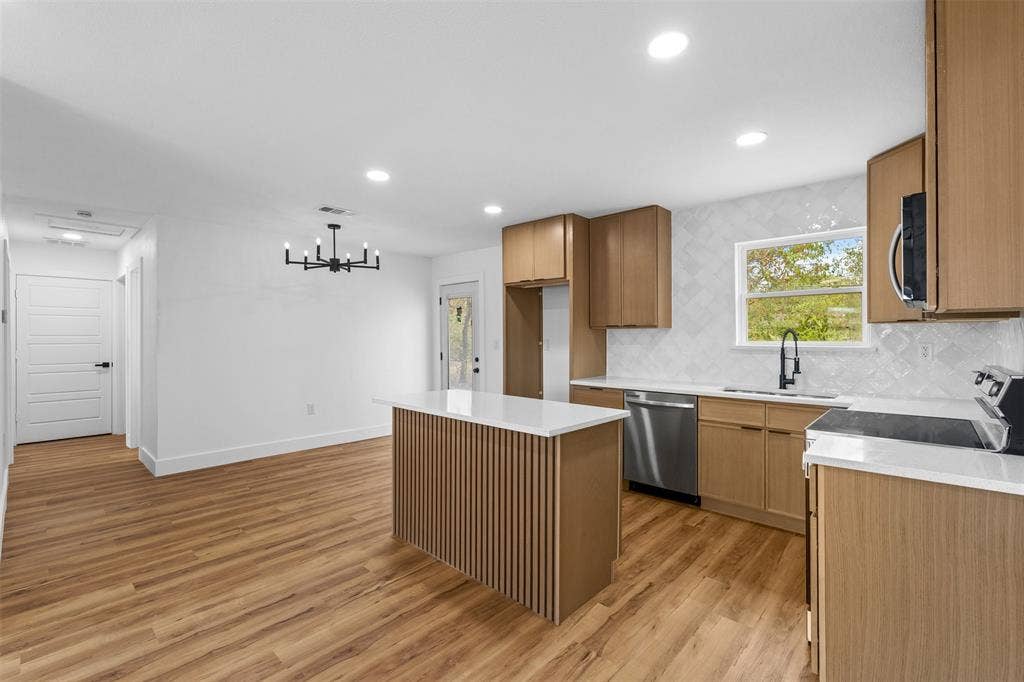 565 alcorn Avenue, Dallas, TX 75217 Open-concept kitchen and dining area featuring wood-finish flooring, a kitchen island with slatted paneling, light wood cabinetry, white countertops, and stainless steel appliances