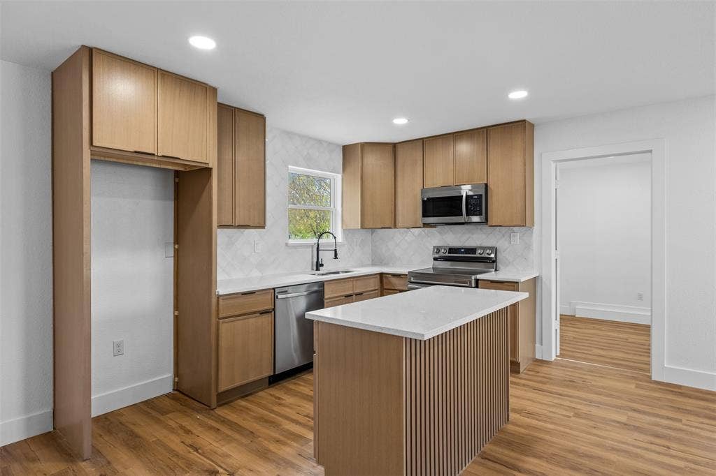 565 alcorn Avenue, Dallas, TX 75217 Modern kitchen featuring wood-finish cabinetry, stainless steel appliances, a white quartz countertop island, and wood-finish flooring