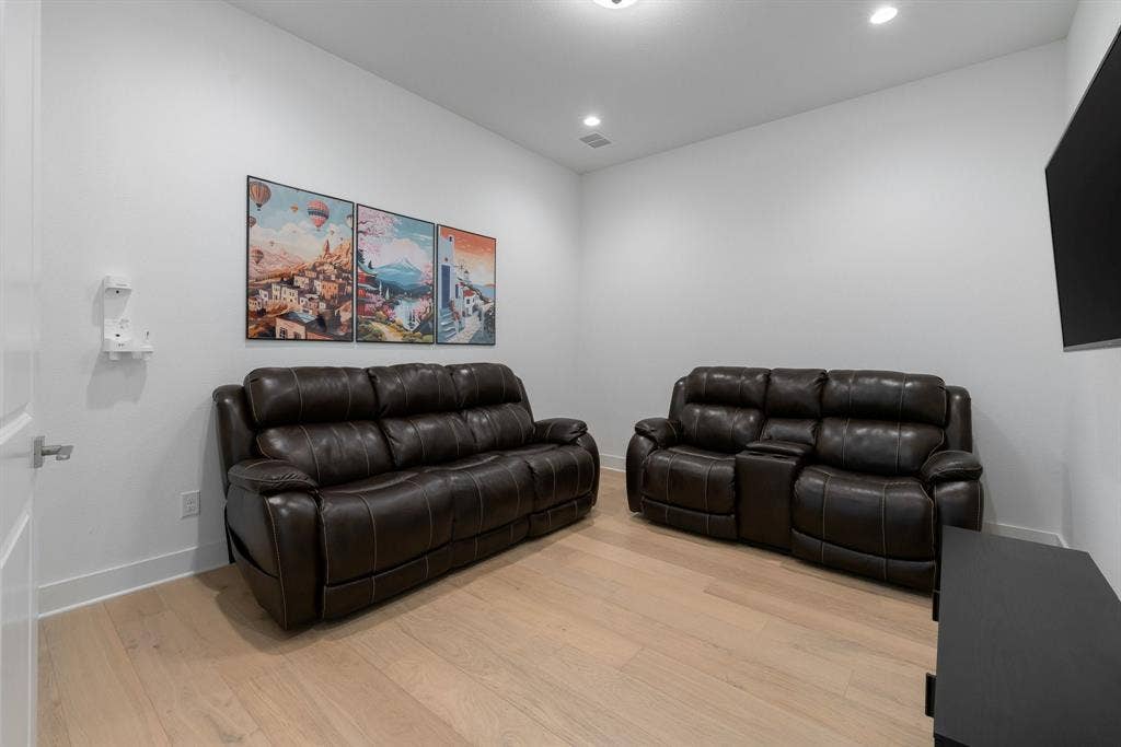 Recessed lighting illuminates this room featuring wood-finish flooring and a wall-mounted television