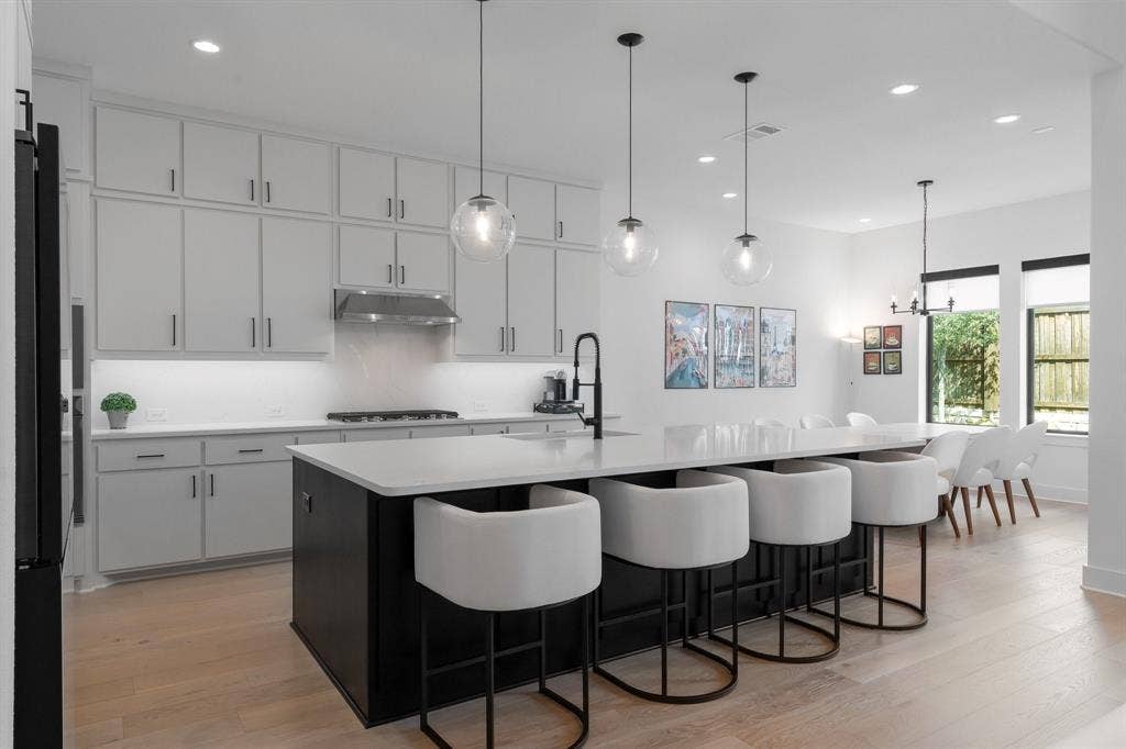 Modern kitchen featuring light-toned cabinetry, a black kitchen island with a white countertop, stainless steel range hood, and light wood-finish flooring