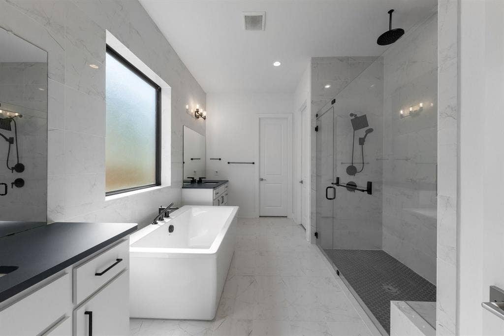 Spacious bathroom featuring a freestanding soaking tub, a large walk-in shower with glass enclosure, dual vanity sinks, white cabinetry, and matte black fixtures throughout