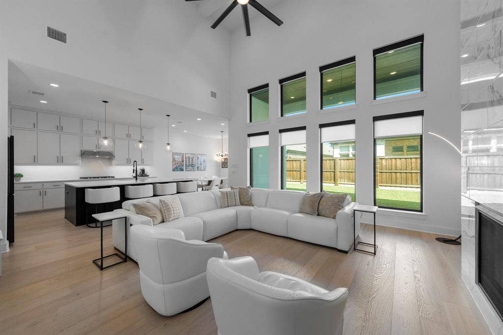 Vaulted ceiling with a ceiling fan, light wood-finish flooring, full-height windows, a modern fireplace, and a kitchen featuring an island with built-in seating