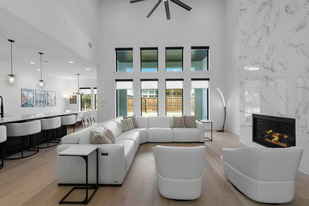 Vaulted ceiling with a ceiling fan, floor-to-ceiling windows, full-height fireplace with stone-finish surround, wood-finish flooring, and built-in kitchen island seating