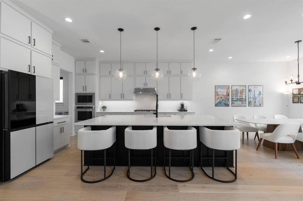 Gourmet kitchen with an expansive island, light wood-finish flooring, white cabinetry, integrated double ovens, and recessed lighting
