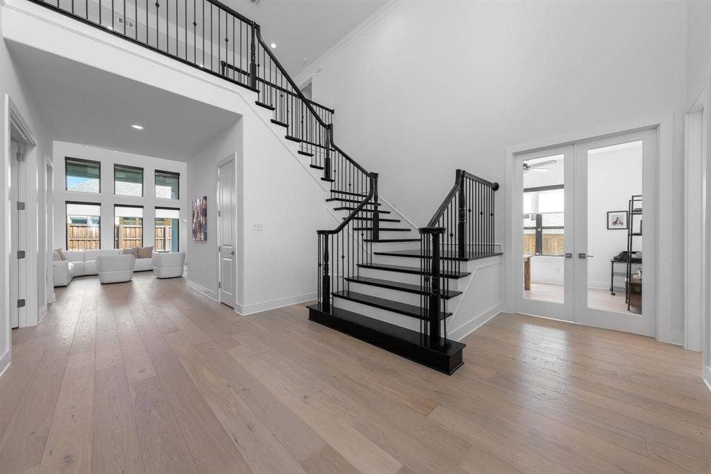Sweeping staircase with black wrought iron balusters, light wood-finish flooring, and a two-story ceiling