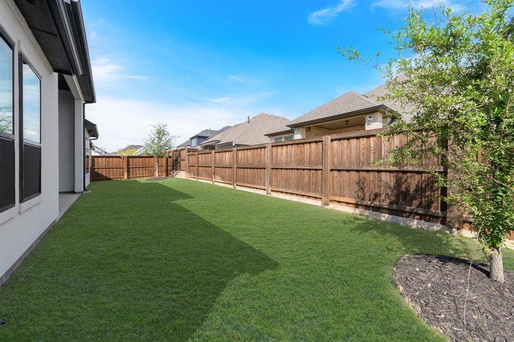 Expansive grassy yard with a privacy fence, exterior siding, and a landscaped bed
