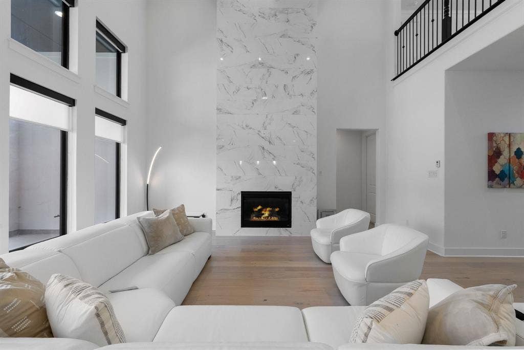 Two-story living area with high ceilings, a grand fireplace featuring a floor-to-ceiling stone-look surround, and wood-finish flooring