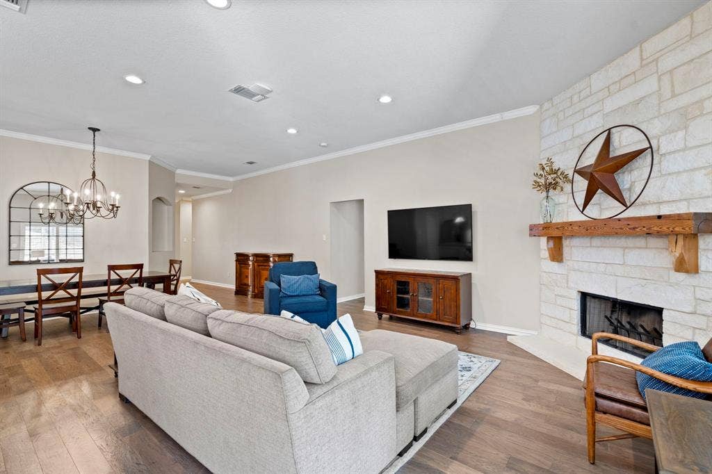 11701 Cambria Court, Fort Worth, TX 76008 Stone-clad fireplace with a natural wood mantel, wood-finish flooring, recessed lighting, and a chandelier in the dining area