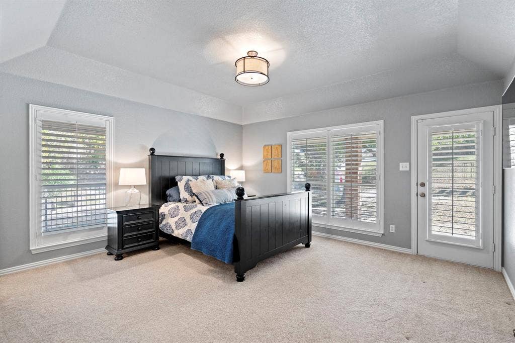 11701 Cambria Court, Fort Worth, TX 76008 Vaulted ceiling, two large windows with plantation shutters, a glass-paneled exterior door with plantation shutters, and light-toned carpet flooring