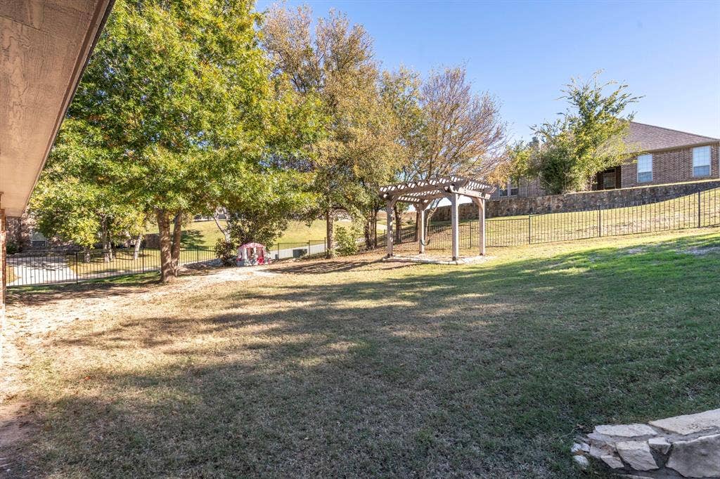 11701 Cambria Court, Fort Worth, TX 76008 Spacious backyard featuring a pergola, mature trees, and a black wrought iron fence