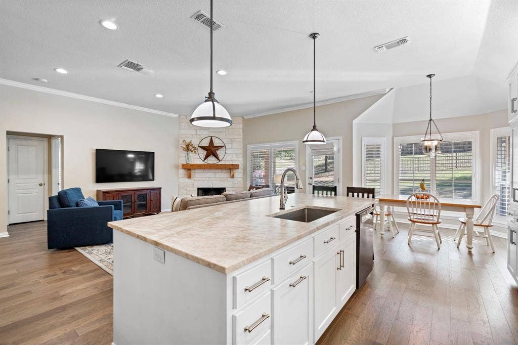 11701 Cambria Court, Fort Worth, TX 76008 Kitchen island with an undermount sink, pendant lighting, wood-finish flooring, white cabinetry, and a stone fireplace