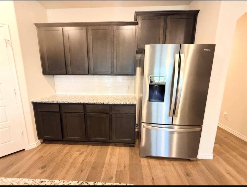 Dark-finish shaker-style cabinetry, speckled stone countertop, white subway tile backsplash, stainless steel french-door refrigerator, and wood-finish flooring