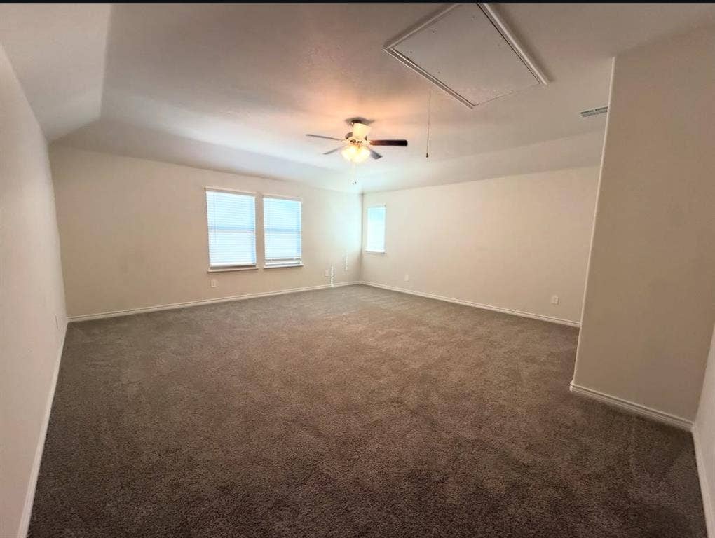 Spacious room featuring a tray ceiling, neutral wall tones, wall-to-wall carpeting, three windows, and a ceiling fan with integrated lighting