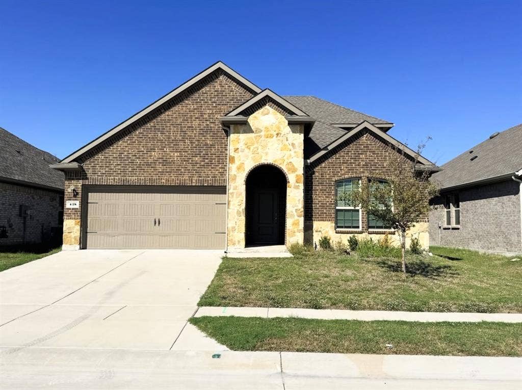 Exterior featuring a brick facade with stone masonry accents, an arched covered entryway, a gabled roofline, and an attached two-car garage