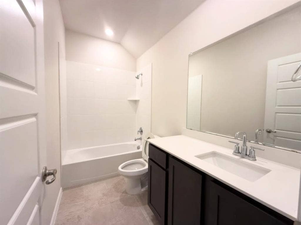 Bathroom featuring a dark-finish vanity with a light-toned countertop, integrated rectangular sink, large wall-mounted mirror, and a tub-shower combination with light-toned wall tile