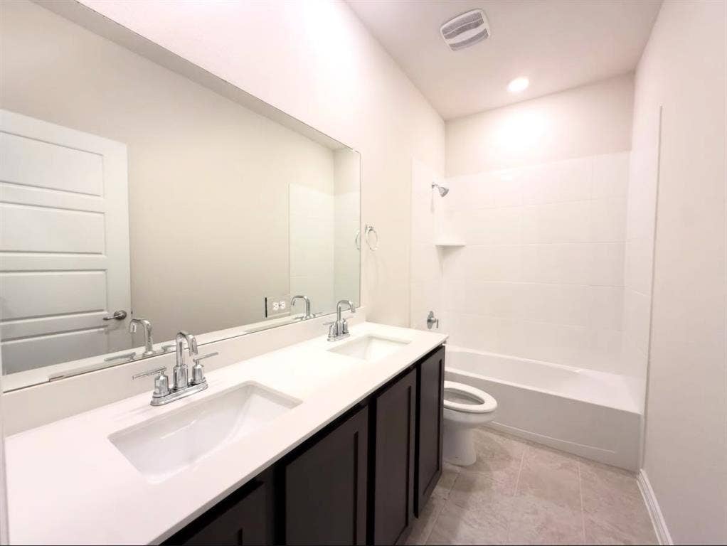 Dual-sink vanity with white composite countertop, large wall-spanning mirror, dark cabinetry, and tile flooring