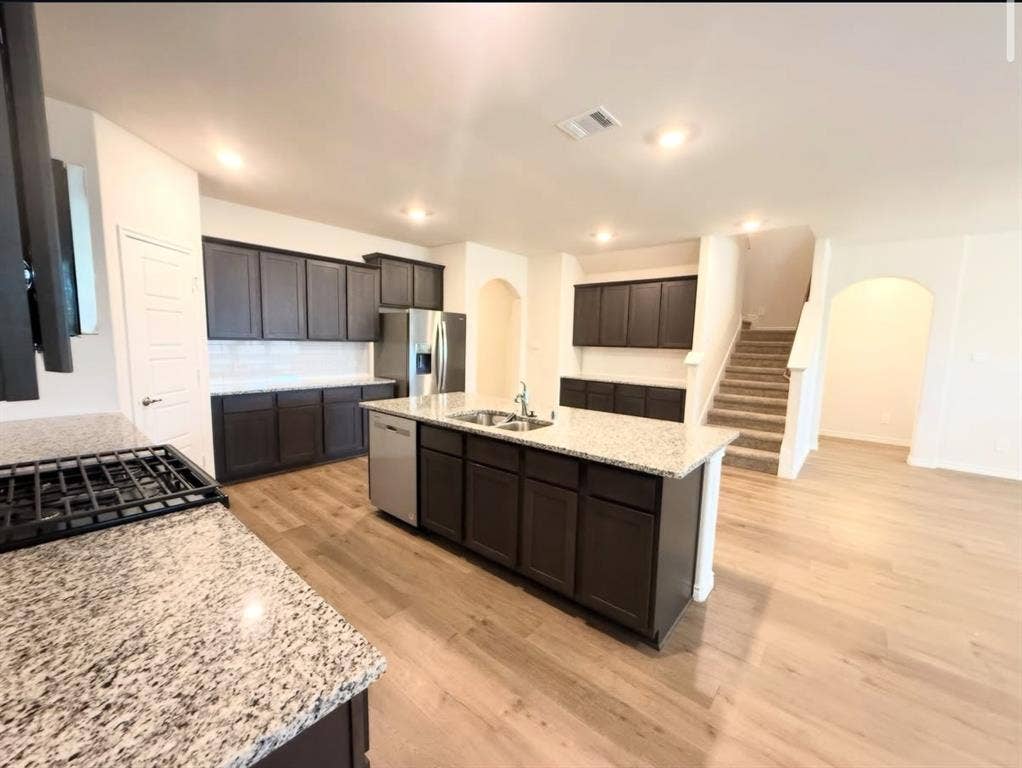 Kitchen featuring dark cabinetry, stone-surface countertops, wood-finish flooring, a central island with integrated stainless steel appliances, and recessed lighting