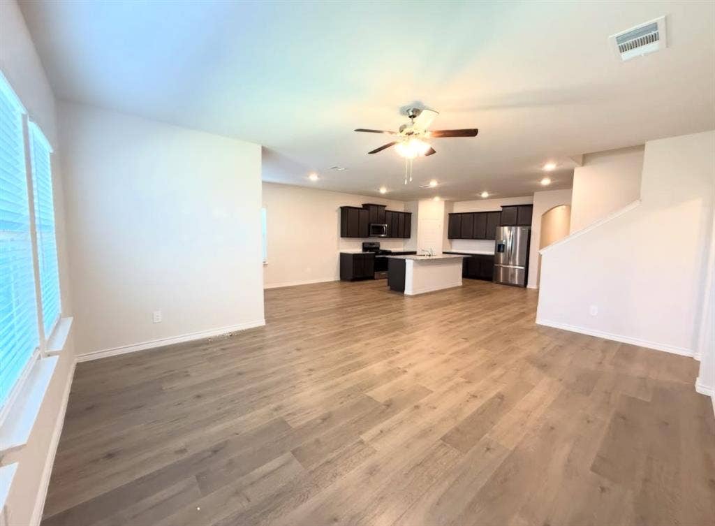Open-concept interior featuring wood-finish flooring, dark-toned cabinetry, a central kitchen island, recessed lighting, and a ceiling fan