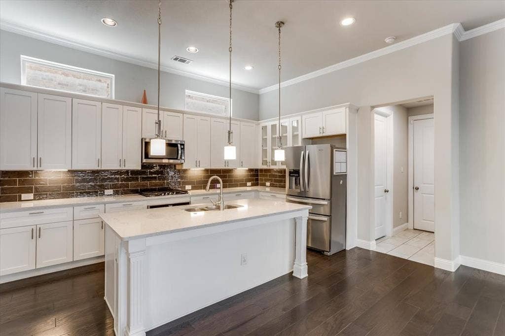 Kitchen featuring a central island with a sink, white cabinetry, integrated stainless steel appliances, and dark wood-finish flooring