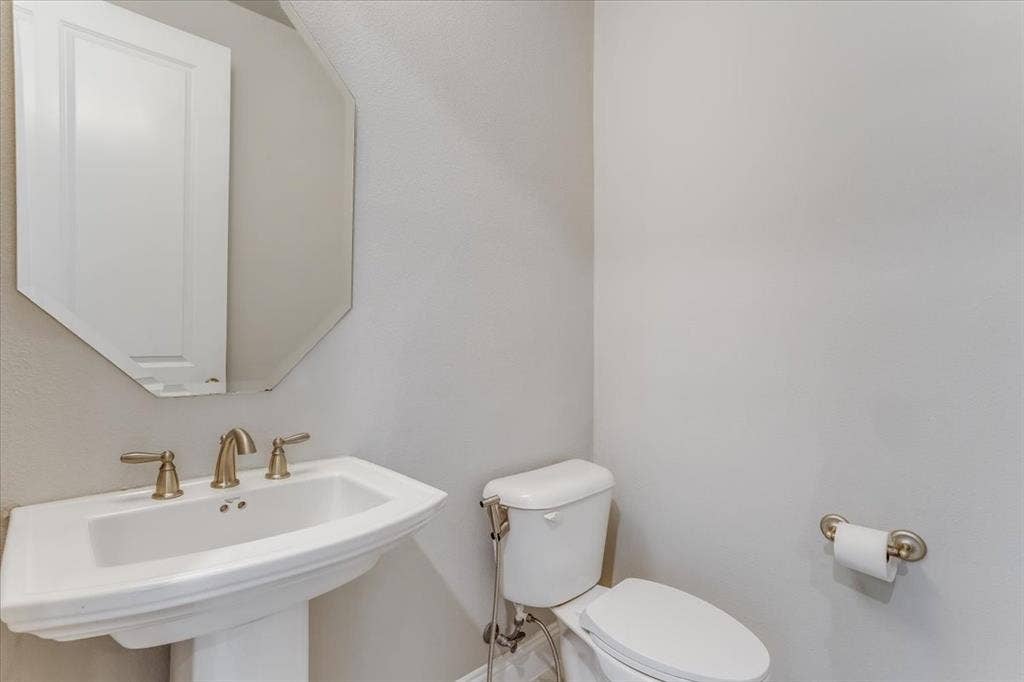 Pedestal sink with brass-finish faucet, octagonal wall mirror, and toilet with brass-finish bidet attachment