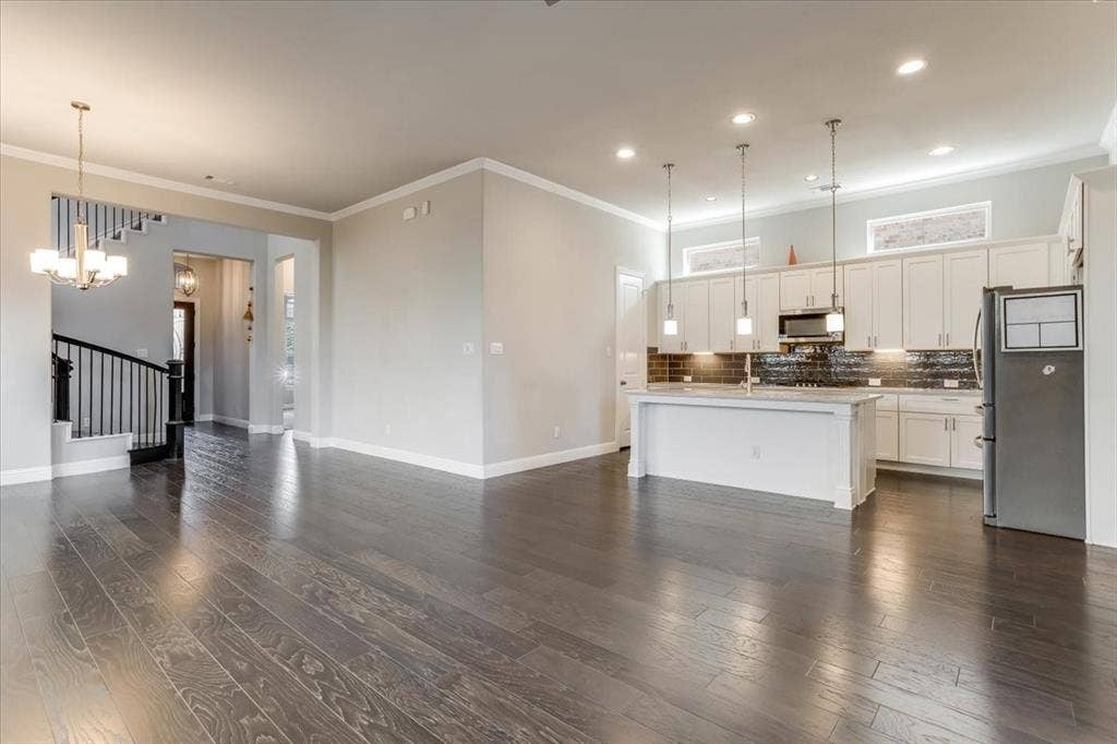 Wood-finish flooring throughout, kitchen with white cabinetry, stainless steel appliances, pendant lighting, and a kitchen island