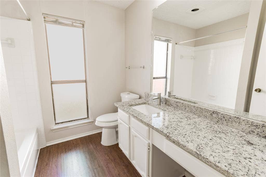 1328 Colmar Drive, Plano, TX 75023 Bathroom featuring a built-in tub with shower, wood-finish flooring, and a vanity with a white basin sink and speckled countertop