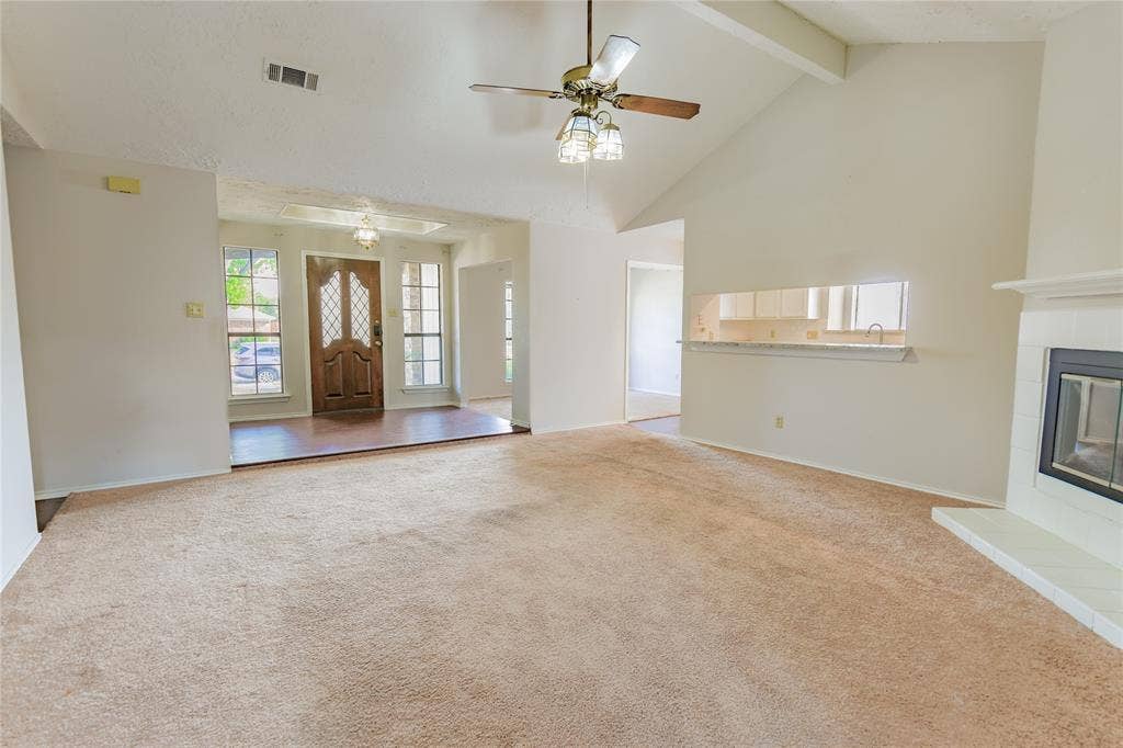 1328 Colmar Drive, Plano, TX 75023 Spacious living area featuring a vaulted ceiling with exposed beams, ceiling fan, and a fireplace with a white tile hearth