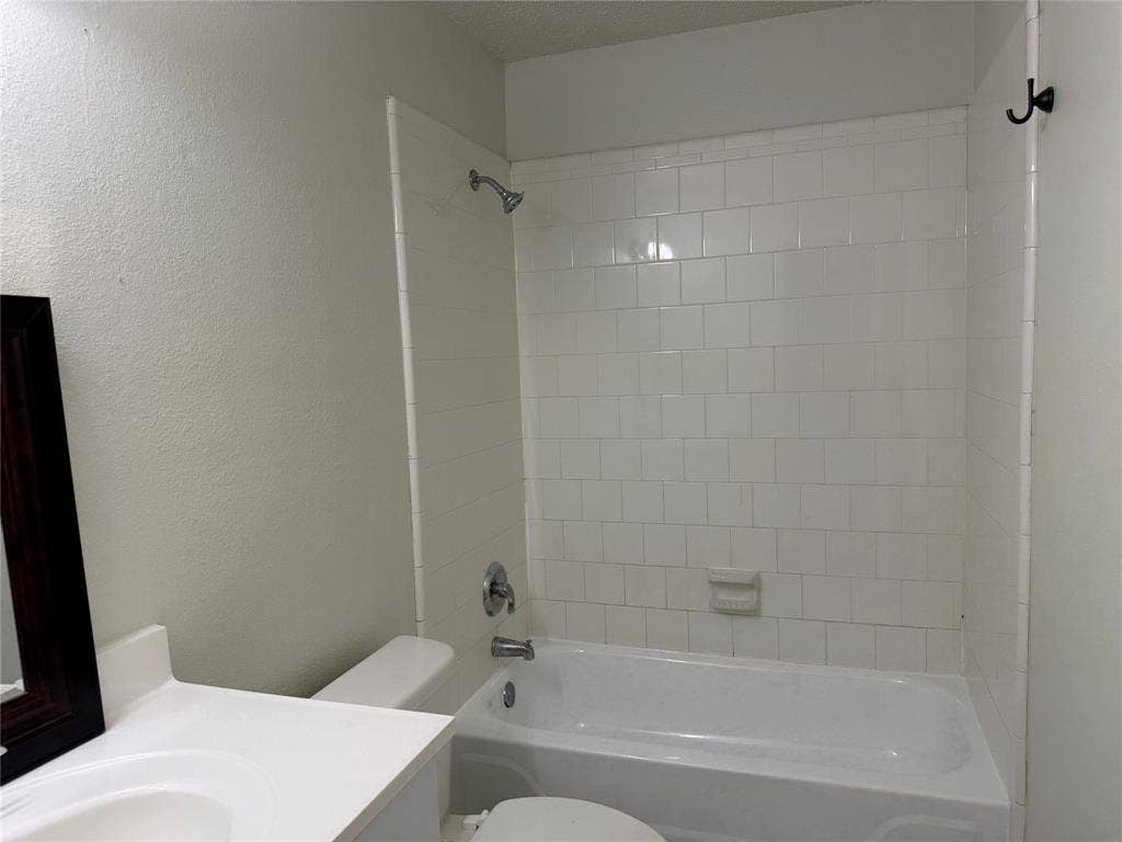 White tile shower surround with chrome fixtures, integrated bathtub, and a white vanity with an undermount sink