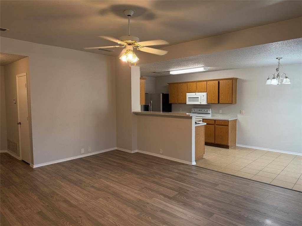 Wood-finish flooring, ceiling fan with integrated lighting, kitchen featuring wood cabinetry, white countertops, and white appliances, and a tiled dining area