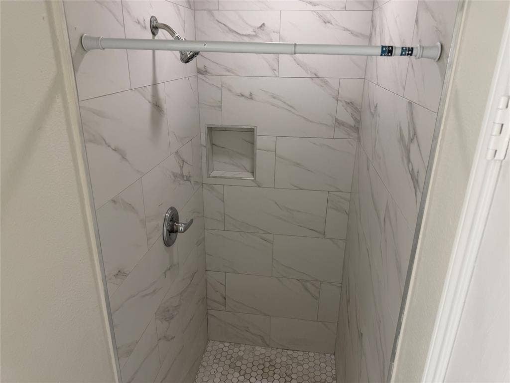 Tile shower featuring a recessed niche, chrome fixtures, and a white penny tile floor