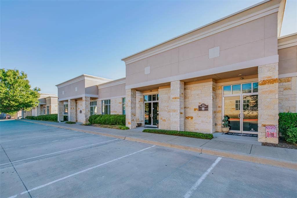 3900 S Stonebridge Drive, #203, McKinney, TX 75070 Stone and stucco facade commercial building with multiple storefronts, extensive paved parking, and mature perimeter landscaping
