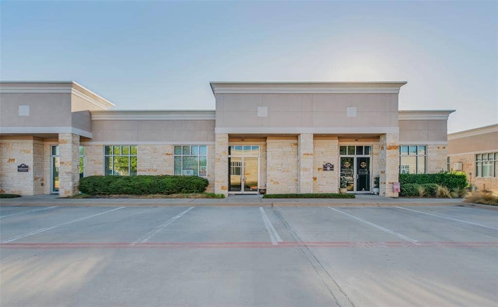 3900 S Stonebridge Drive, #203, McKinney, TX 75070 Commercial building featuring stone and stucco exterior, multiple glass storefront entries, extensive windows, and a paved parking lot with marked spaces