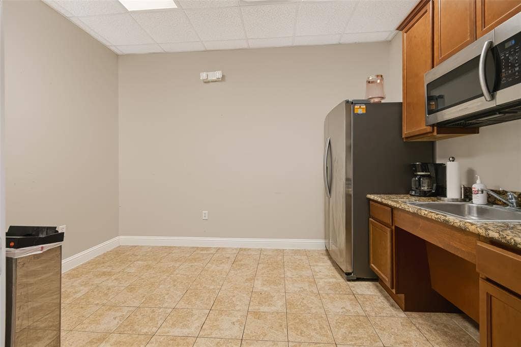 3900 S Stonebridge Drive, #203, McKinney, TX 75070 Kitchenette featuring tile flooring, wood-finish cabinetry, stainless steel appliances, and a solid surface countertop with an integrated sink