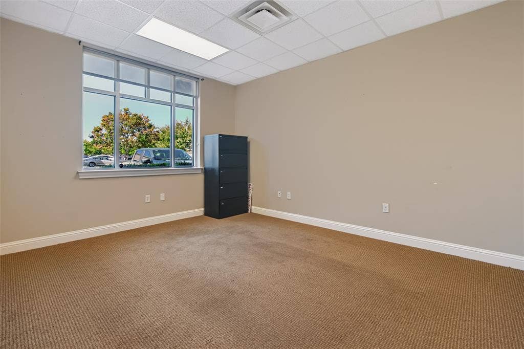 3900 S Stonebridge Drive, #203, McKinney, TX 75070 Carpeted room featuring a large window with multiple panes, drop ceiling with integrated lighting, and neutral wall tones