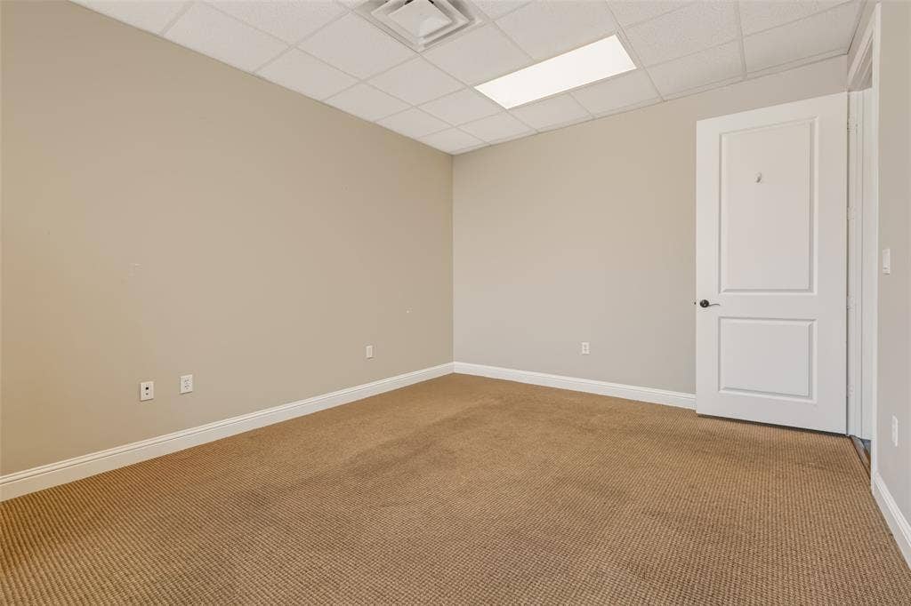 3900 S Stonebridge Drive, #203, McKinney, TX 75070 Neutral wall paint, drop ceiling with integrated lighting, textured carpet flooring, white trim, and a paneled interior door with dark hardware